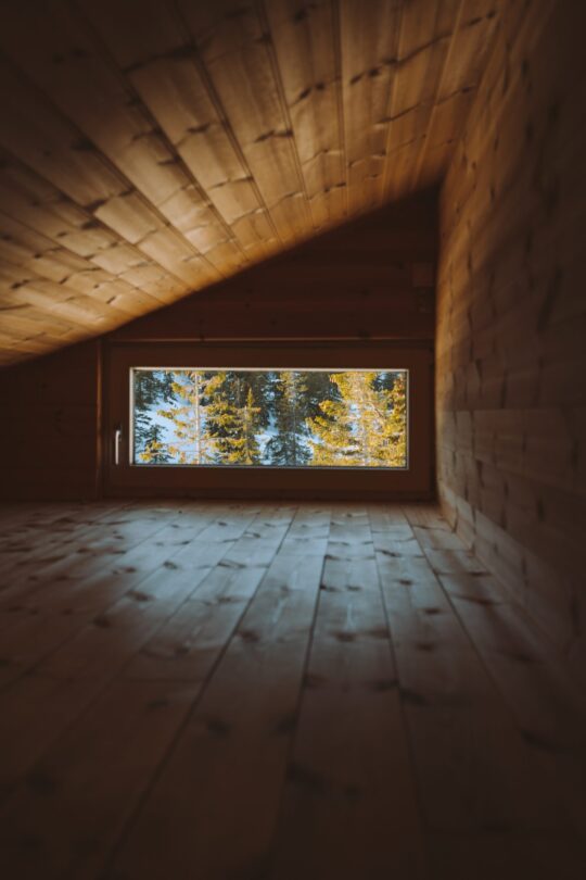 A vertical shot of a cozy attic with a window with the view of a forest covered with snow in Norway